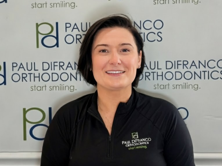 Orthodontic assistant smiling in front of Paul DiFranco Orthodontics sign, showcasing dedication to patient care in Palos Hills, IL.