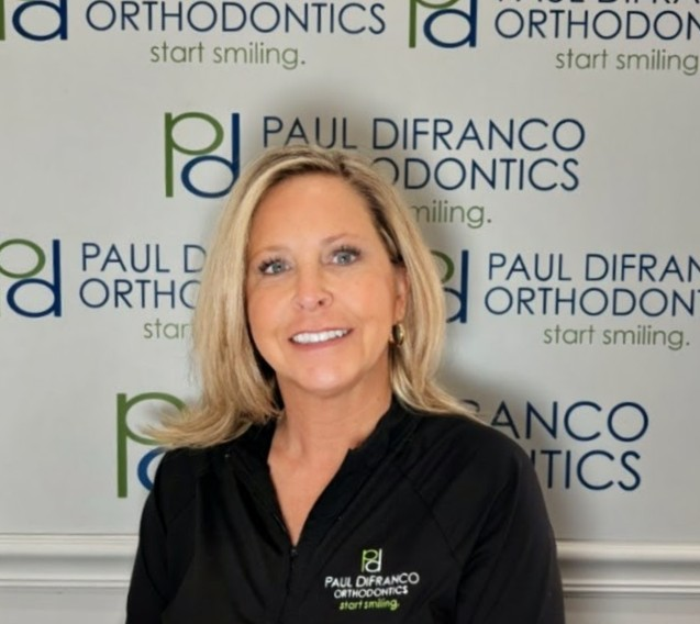 Denise, Financial Coordinator at Paul DiFranco Orthodontics, smiling in front of branded backdrop, emphasizing personalized orthodontic care in Palos Hills, IL.