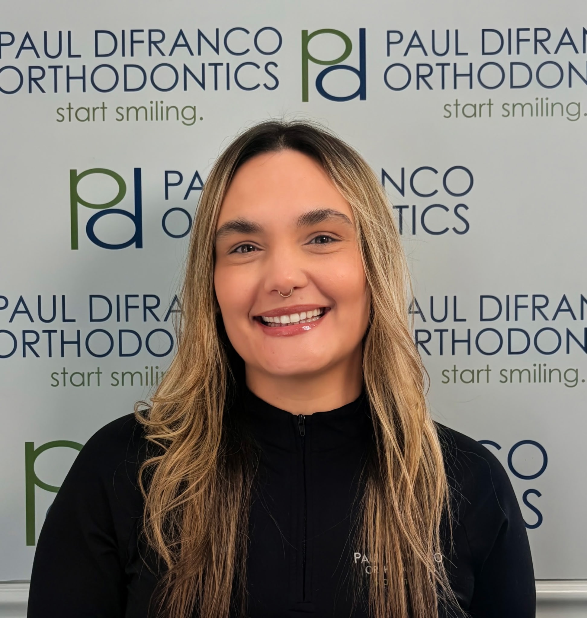 Jessica, Treatment Coordinator at Paul DiFranco Orthodontics, smiling in front of the practice's logo, promoting personalized orthodontic care in Palos Hills, IL.