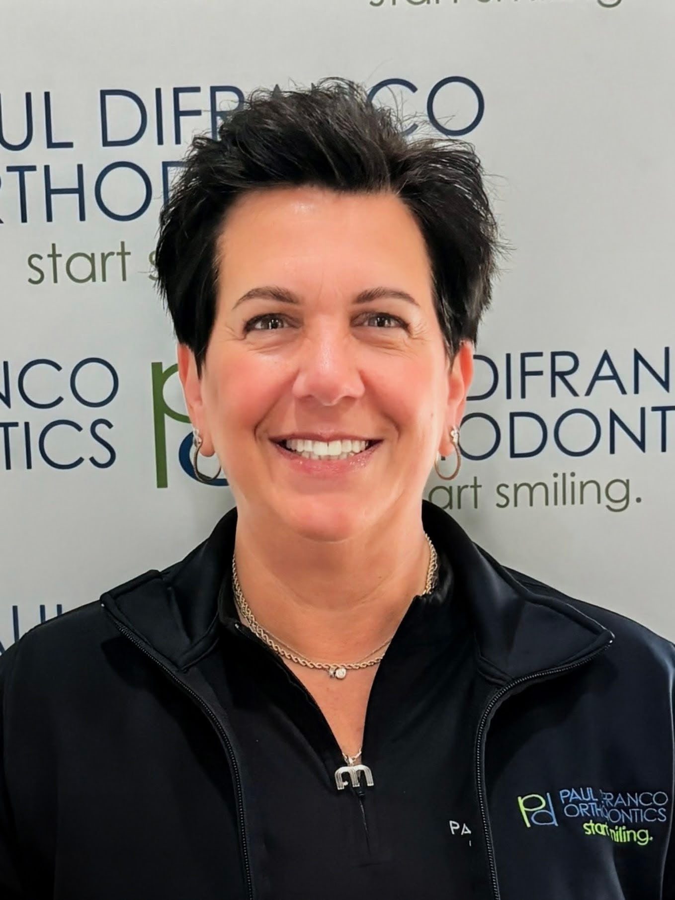 Michelle, office manager at Paul DiFranco Orthodontics in Palos Hills, IL, smiling in front of branded backdrop, showcasing dedication to patient care and orthodontics.