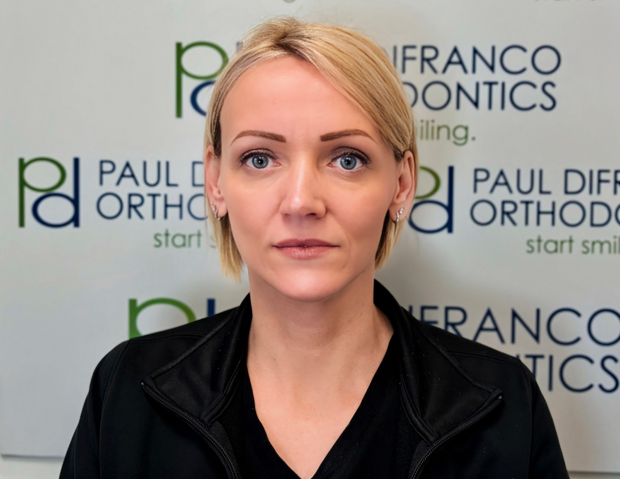 Haley, Scheduling Coordinator at Paul DiFranco Orthodontics, smiling in front of branded office backdrop, emphasizing her role in patient care and office efficiency in Palos Hills, IL.